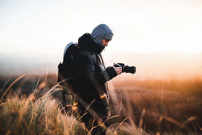 Fotograf w kurtce robi zdjęcia na łące o świcie