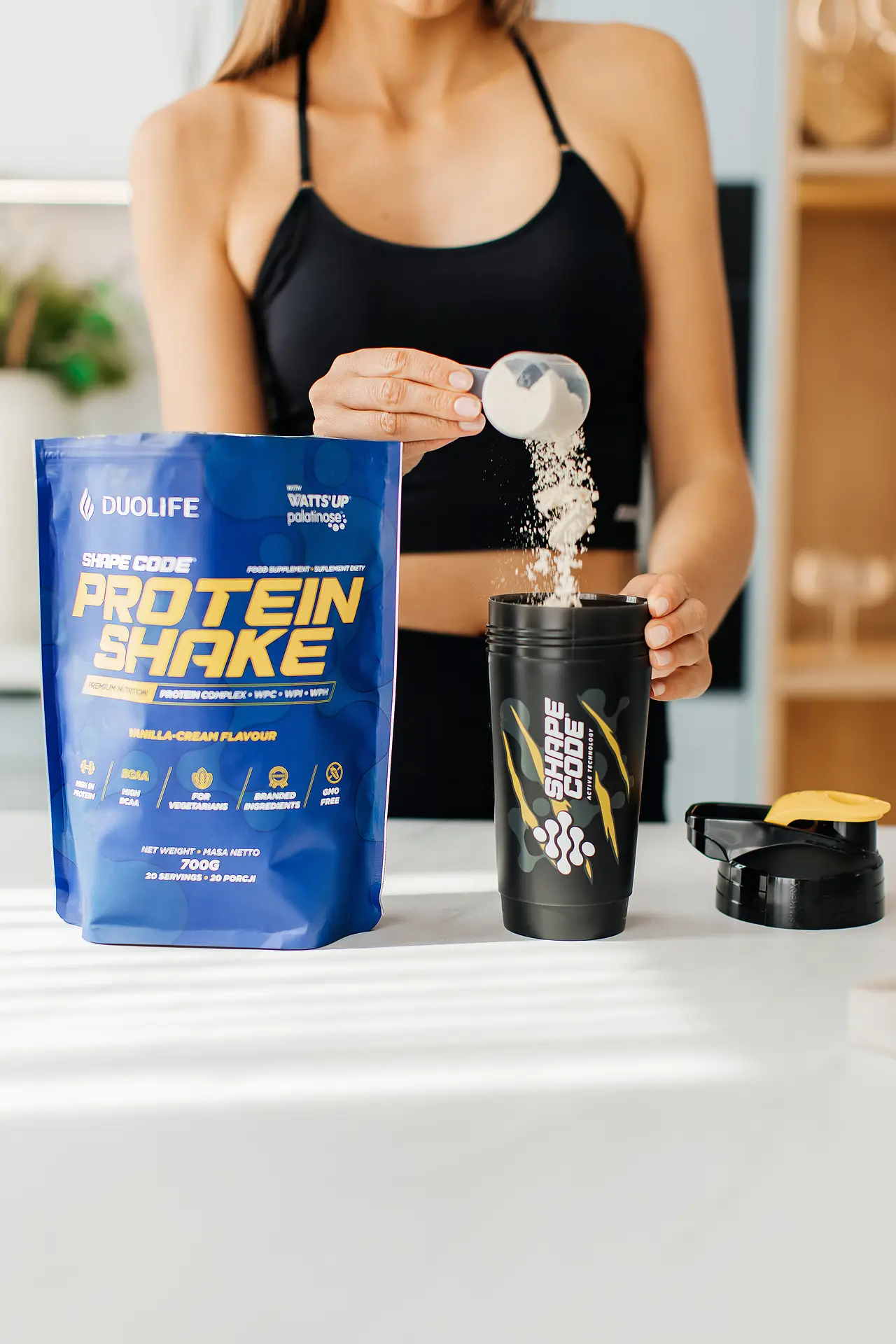 Fotografia produktowa odżywki proteinowej z modelką przygotowującą shake w shakerze
